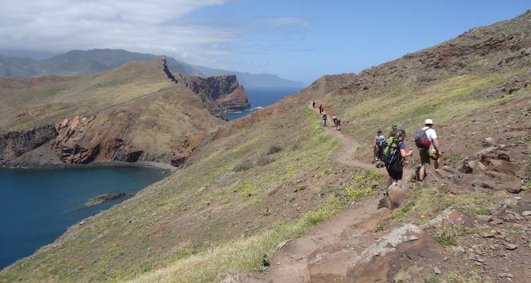 Grupo de excursionistas en un sendero montañoso costero con vistas al mar.