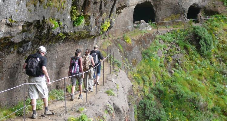 Grupo de excursionistas caminando por un sendero estrecho junto a acantilados con cuevas.
