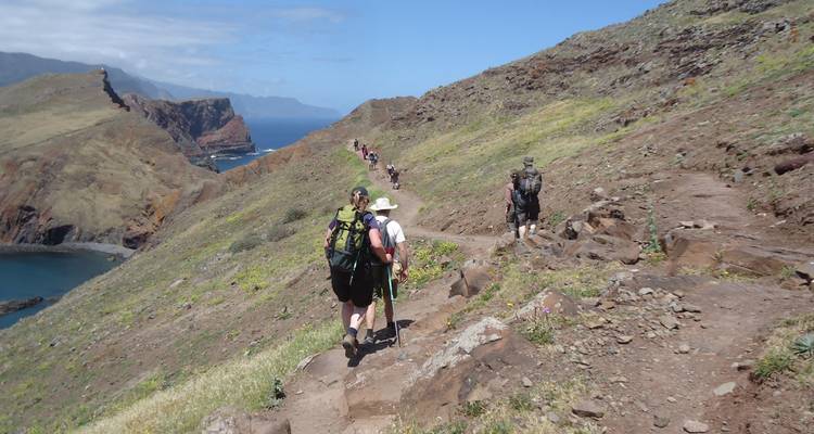 Excursionistas caminando por una ruta de senderismo costera con vistas al océano.