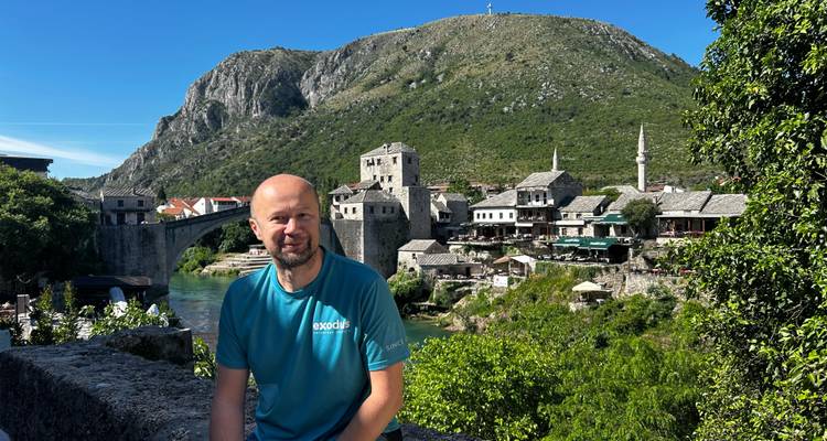 Ein Reisender sitzt neben einer Steinmauer mit Blick auf die historische alte Brücke von Mostar und den Fluss.