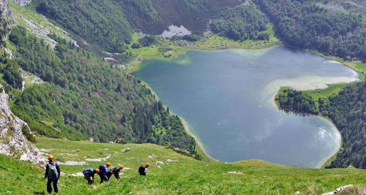 Wanderer, die einen steilen grasbewachsenen Hang oberhalb eines Sees erklimmen.