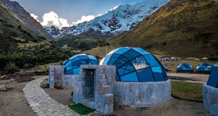 Cabañas futuristas de cúpula geodésica de cristal azul ubicadas en un verde valle andino bajo picos cubiertos de nieve.