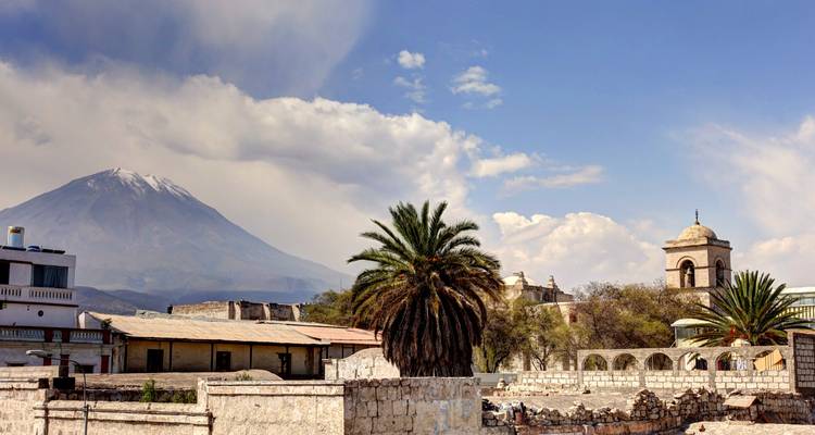 Vista de una montaña y arquitectura colonial con una palmera.
