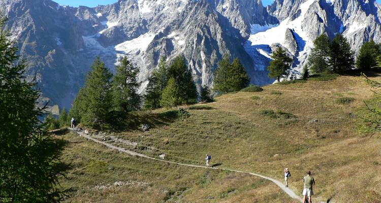 Randonneurs sur un sentier avec des montagnes enneigées au loin.