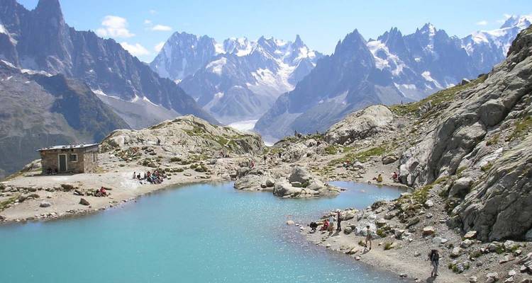 Paysage de montagne pittoresque avec un lac turquoise et des personnes se reposant à proximité.