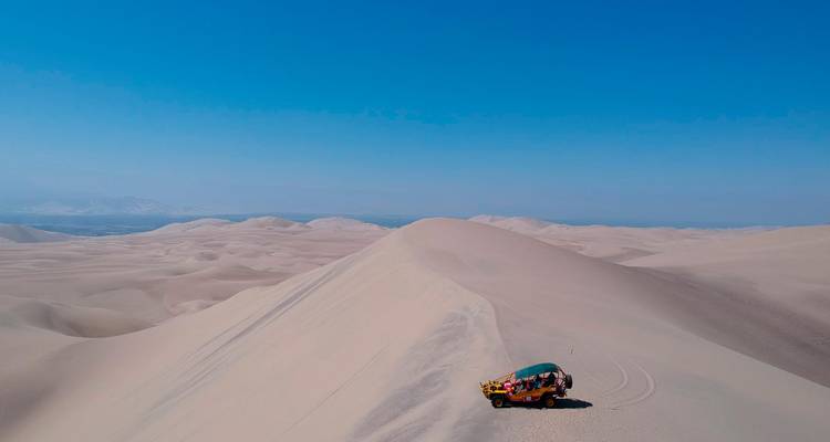 Vasto paisaje desértico con un vehículo solitario en una duna.