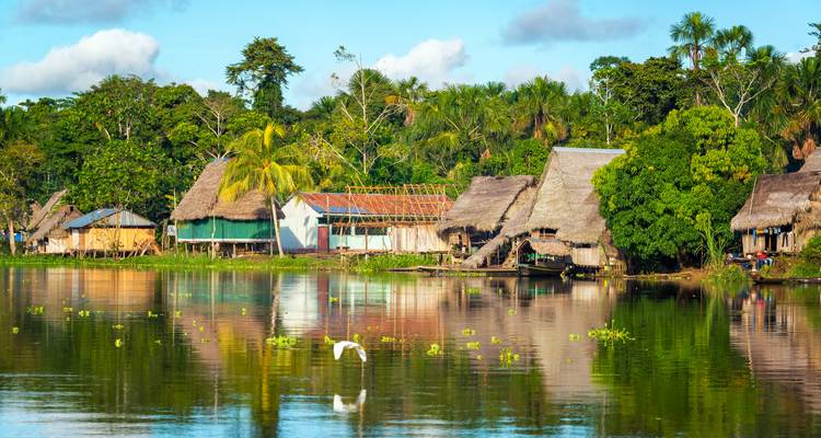 Village au bord de la rivière avec des huttes traditionnelles au toit de chaume entourées d'une végétation luxuriante.