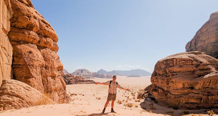 Reiziger spreidt armen vol vreugde uit in de enorme zandwoestijn omgeven door imposante rode rotsen in Wadi Rum.