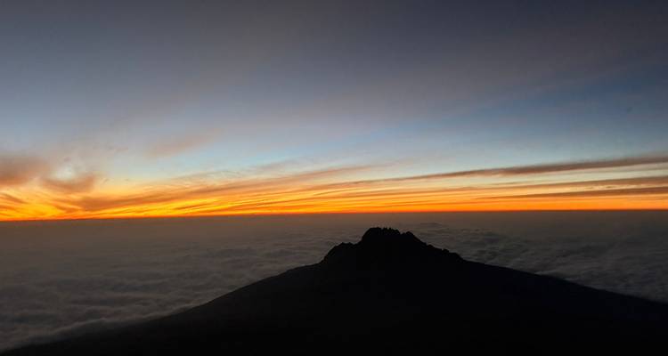 Silhouet van de Kilimanjaro-top boven een zee van wolken bij een levendige zonsopgang.