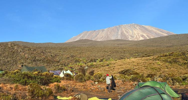 Een klimmer loopt door het ochtendkamp onder de sneeuw bedekte top van de Kilimanjaro.