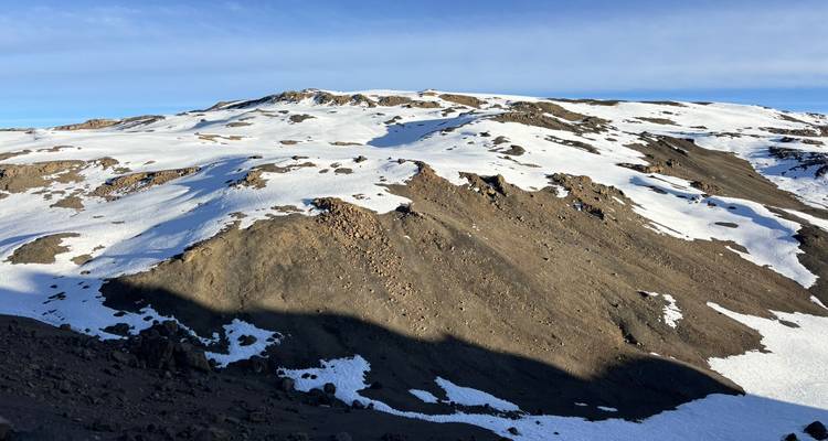 Sneeuwvlekken op een vulkanisch plateau onder een heldere blauwe hemel op de hogere hellingen van Kilimanjaro.