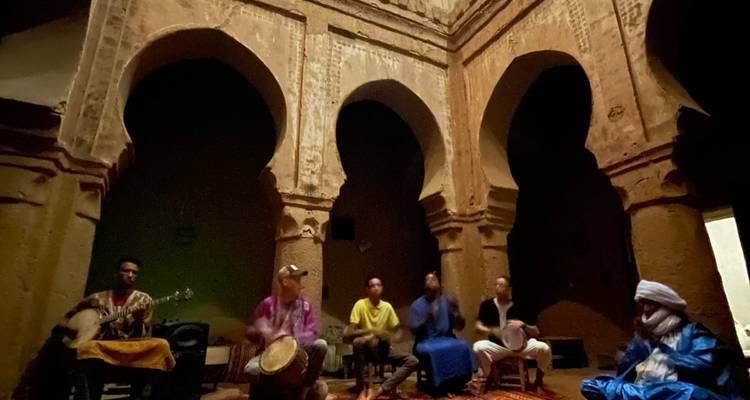 Intérieur marocain traditionnel faiblement éclairé où des musiciens jouent des tambours et du luth au milieu de piliers d'adobe voûtés.
