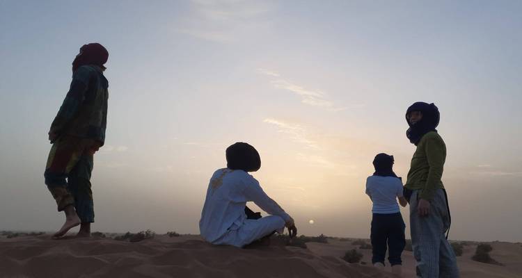 Des voyageurs en silhouette sur une dune de sable observant le soleil couchant dans le Sahara.