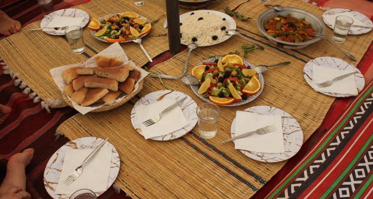 Configuration de repas traditionnel en plein air sur des nattes tissées avec des salades fraîches, du pain et des oranges prêts à partager.