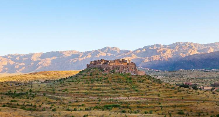 Ancienne kasbah au sommet d'une colline avec un ciel bleu en arrière-plan.