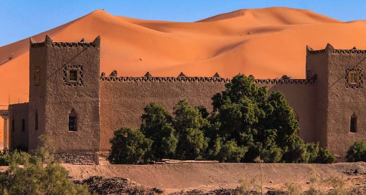 Kasbah marocaine traditionnelle avec des dunes du désert en arrière-plan.