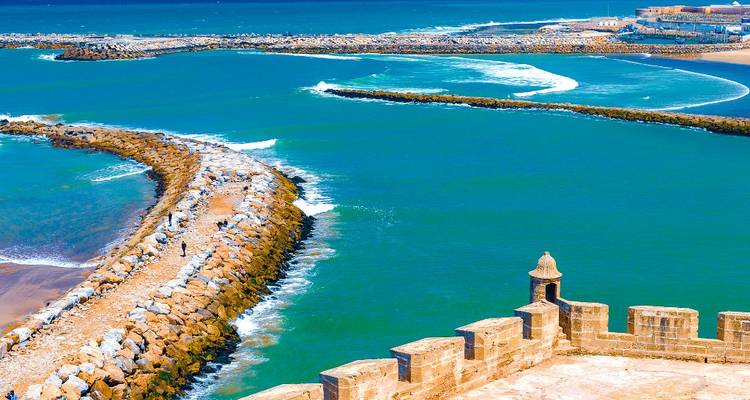 Vue côtière avec une forteresse et des vagues qui se brisent par une journée lumineuse.