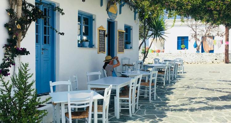 Straßencafé mit weißen Tischen und Stühlen an einem sonnigen Tag.