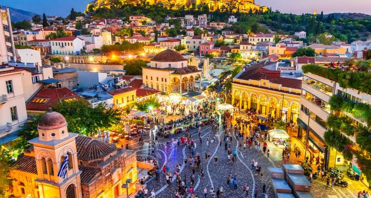 Vue nocturne d'une place animée avec l'Acropole en arrière-plan.