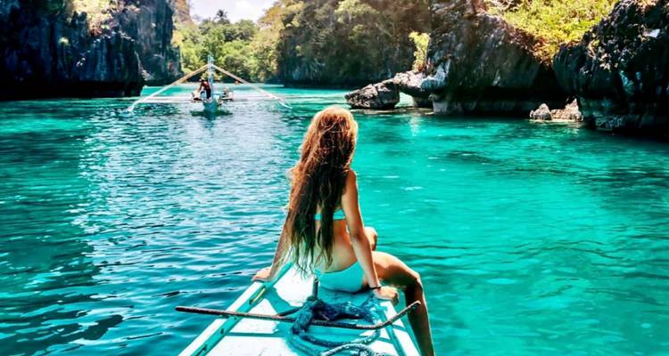 Une femme assise à l'avant d'un bateau dans des eaux cristallines entourée de falaises calcaires.