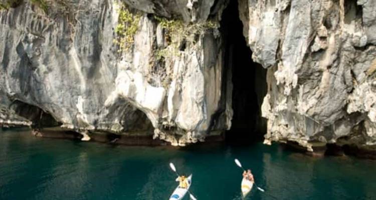 Deux kayakistes pagayant près de l'entrée d'une grotte calcaire.