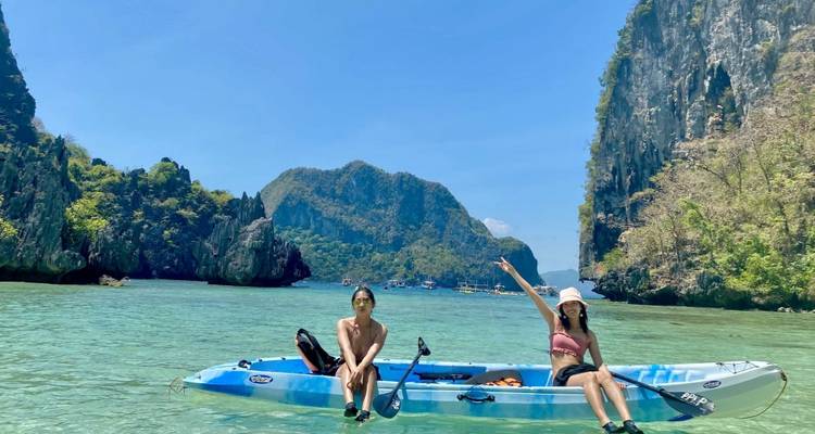 Deux personnes assises dans un kayak dans des eaux claires avec un arrière-plan montagneux.