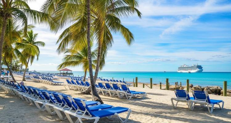 Plage avec des palmiers et des rangées de chaises longues, un bateau de croisière au loin.