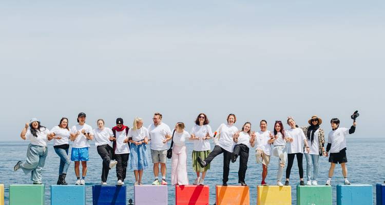 Gran grupo de pie sobre bloques de concreto pintados de colores brillantes junto al mar, posando juguetonamente contra el cielo azul