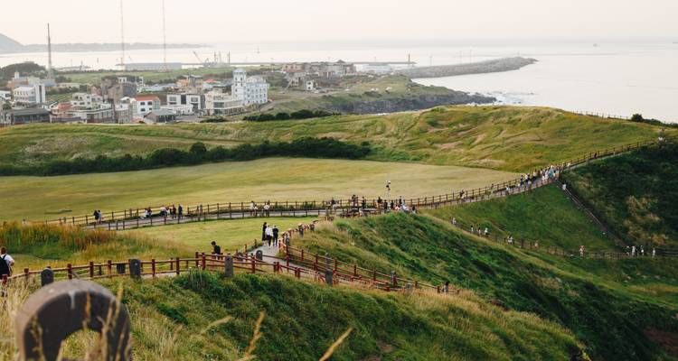 Praderas costeras pintorescas con largas pasarelas de madera llenas de visitantes con vista al mar y pueblo distante