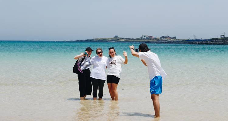 Amigos parados hasta los tobillos en agua turquesa cristalina en una playa de arena blanca haciendo gestos felizmente