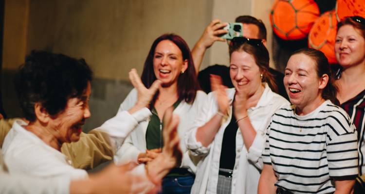 Los viajeros aplauden a una mujer local de edad avanzada durante una experiencia cultural interactiva en interiores