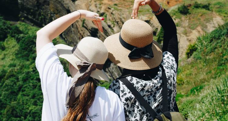 Dos mujeres con sombreros para el sol forman la figura de un corazón con sus brazos mientras contemplan un cráter volcánico