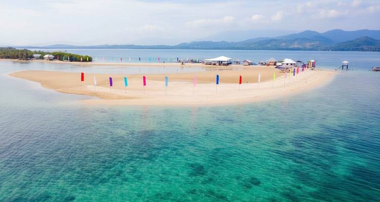 Plage de sable avec drapeaux colorés et eaux claires.