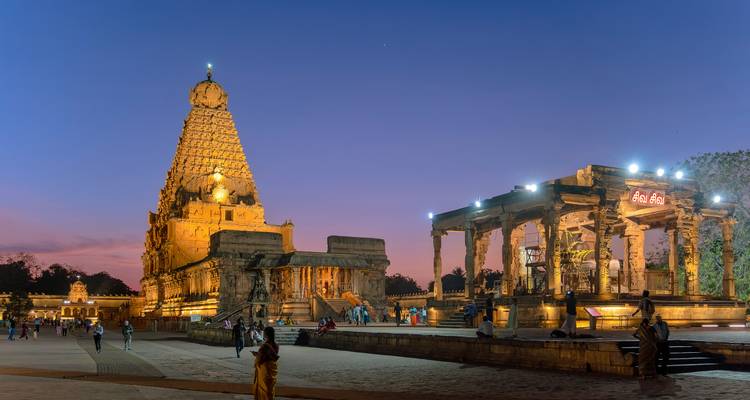 Temple illuminé la nuit avec des touristes autour.