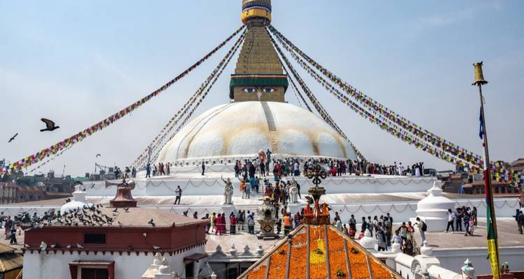 Grand stupa avec drapeaux de prière colorés et visiteurs.