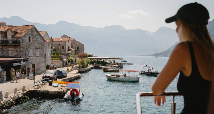 Person on a boat looking at a coastal town and mountains.