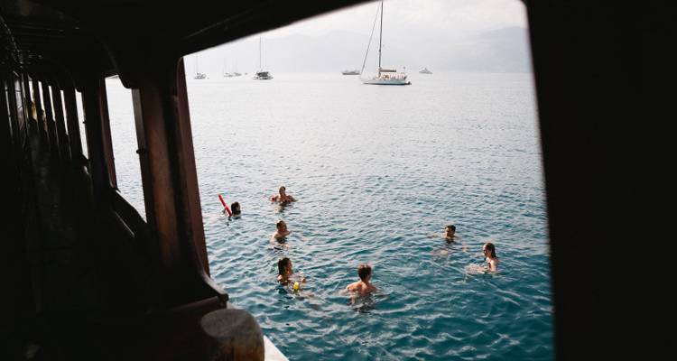 Group of people swimming in the sea with boats in the background.