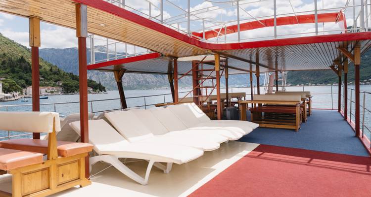 Deck of a boat by a scenic lake with lounge chairs and distant mountains.