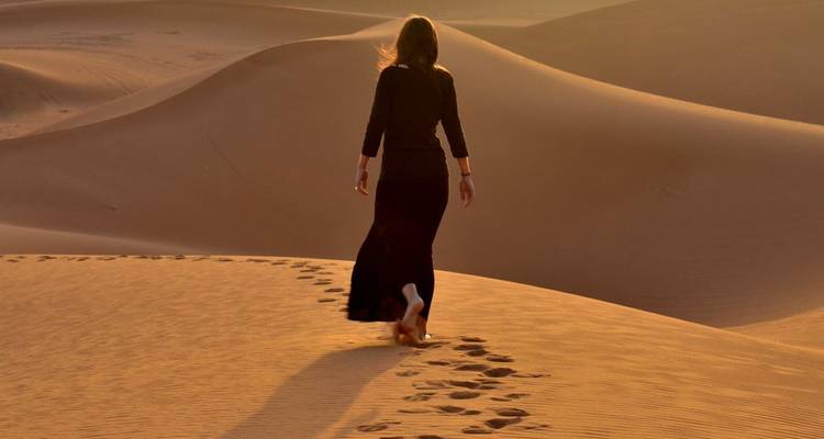 Persona caminando por las dunas de arena, dejando huellas al atardecer.