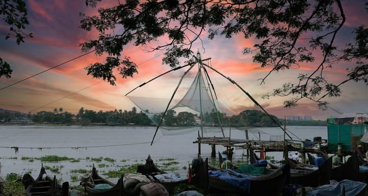 Filets de pêche chinois au bord de la rivière au coucher du soleil, avec des cieux vibrants et des branches d'arbres en silhouette.
