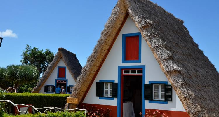 Maisons traditionnelles pittoresques aux toits de chaume avec des bordures colorées sous un ciel lumineux.