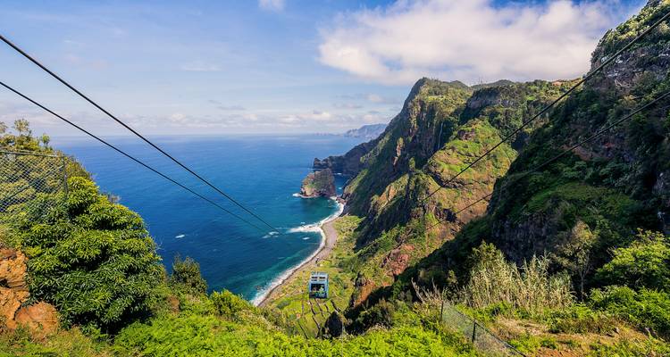 Paysage pittoresque avec téléphérique survolant une végétation luxuriante et des vues sur l'océan.
