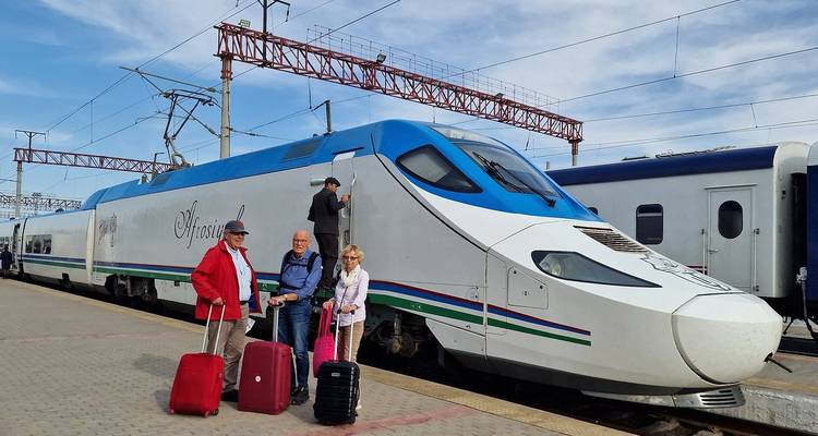 Trois personnes avec des bagages posant devant un train à grande vitesse dans une gare.