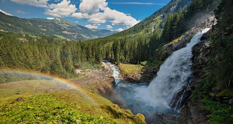 Una vista impresionante de las Cataratas de Krimml en un valle exuberante y verde con un arcoíris visible.