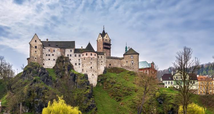 Le château de Loket perché au sommet d'une colline verdoyante sous un ciel nuageux.