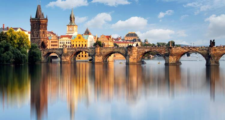 Historic bridge and colorful riverside buildings of Prague reflected perfectly in calm Vltava waters