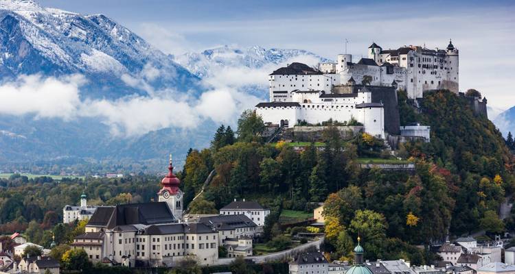 Impressive hilltop fortress dominates a charming European city framed by autumn forests and snowy peaks