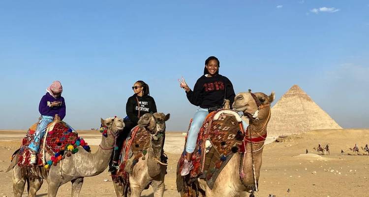 Tres mujeres en camellos con las Pirámides de Giza al fondo.