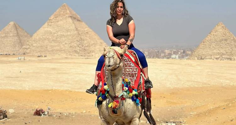 Mujer montando un camello con las Pirámides de Giza en el fondo.
