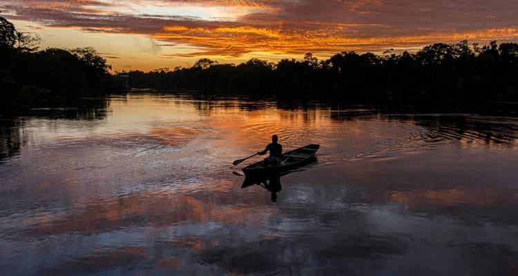Silhouette d'une personne dans un bateau sur une rivière pendant un coucher de soleil dramatique.